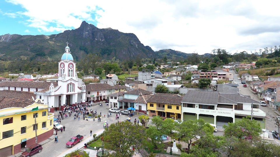 A town square with a prominent church, a mountain in the background, and a mix of residential buildings.