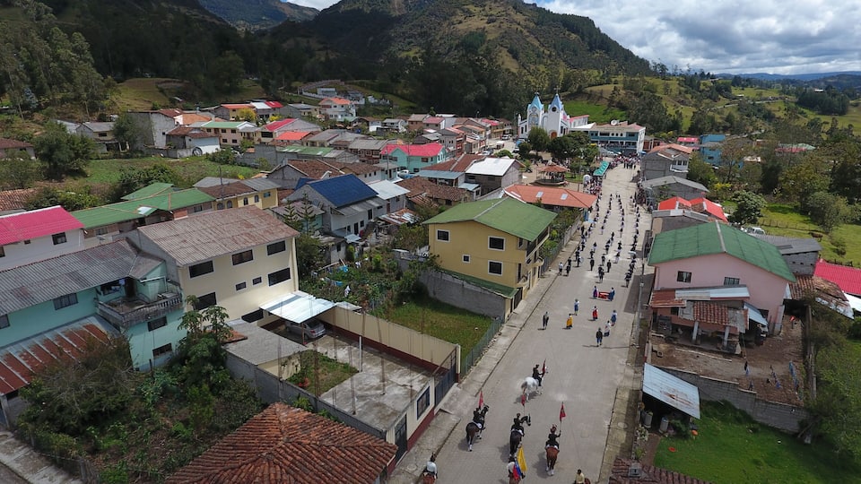 A town with colorful buildings, a central church, and a mountainous backdrop.