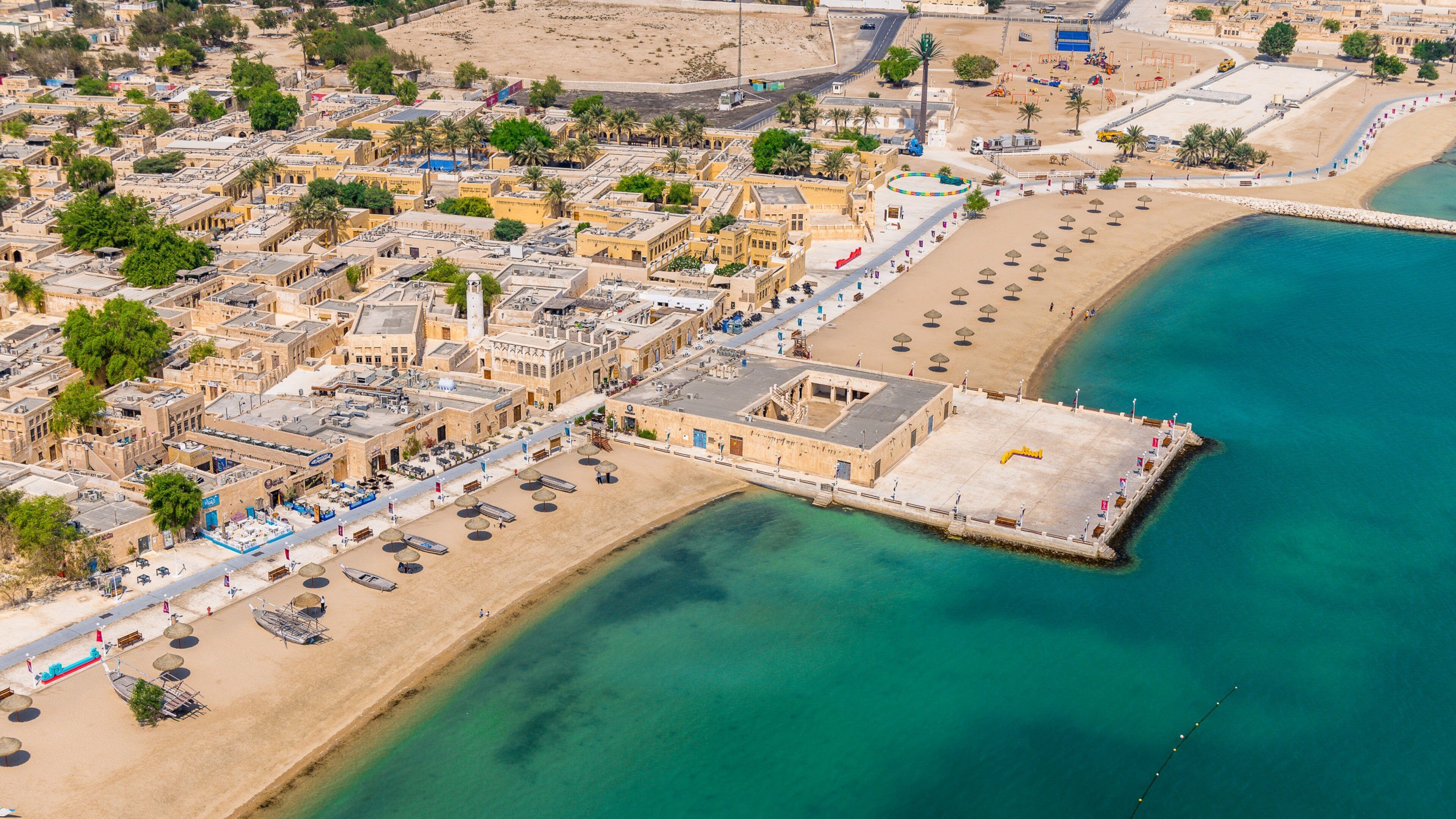 An aerial view of a coastal city with a prominent beach, a fortified harbor, and dense urban architecture.