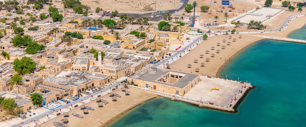 An aerial view of a coastal city with a prominent beach, a fortified harbor, and dense urban architecture.