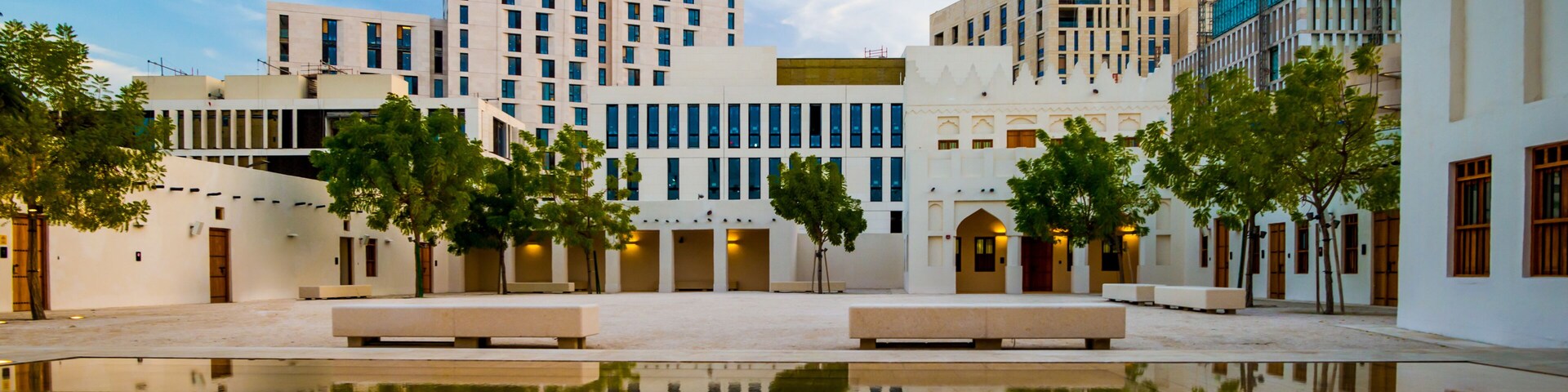 Un patio con un estanque reflectante, edificios modernos y árboles.