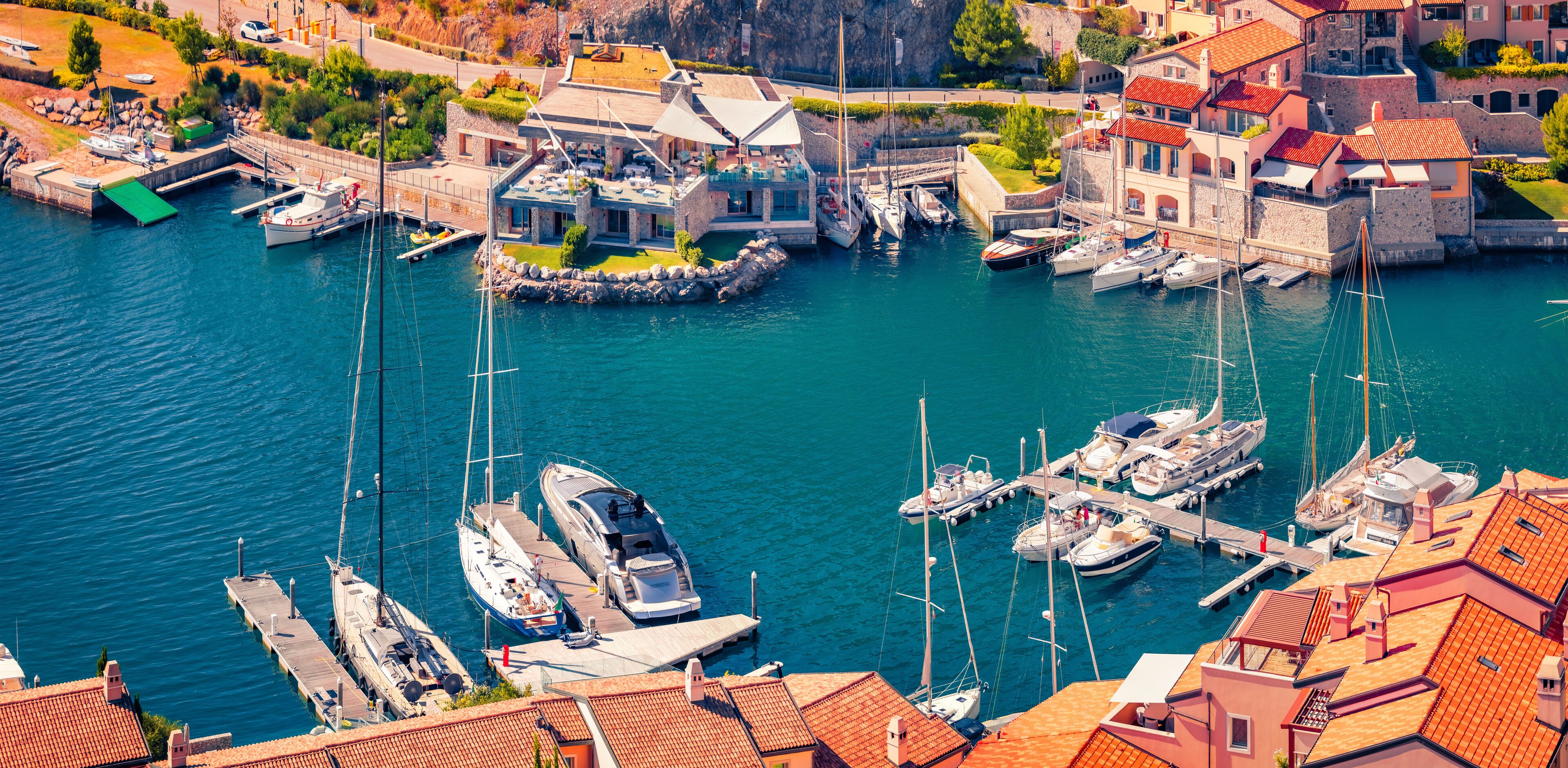 A marina with boats docked, surrounded by buildings with red-tiled roofs.