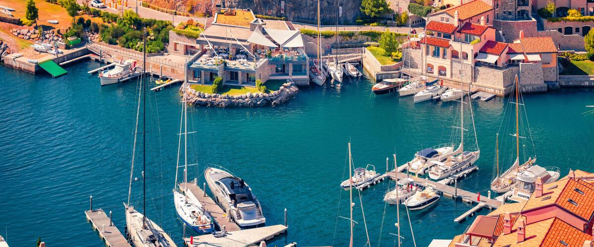 A marina with boats docked, surrounded by buildings with red-tiled roofs.