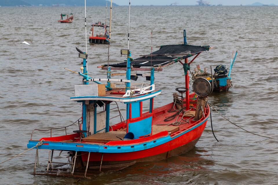Un barco rojo y azul con una red y equipo de pesca en aguas tranquilas.