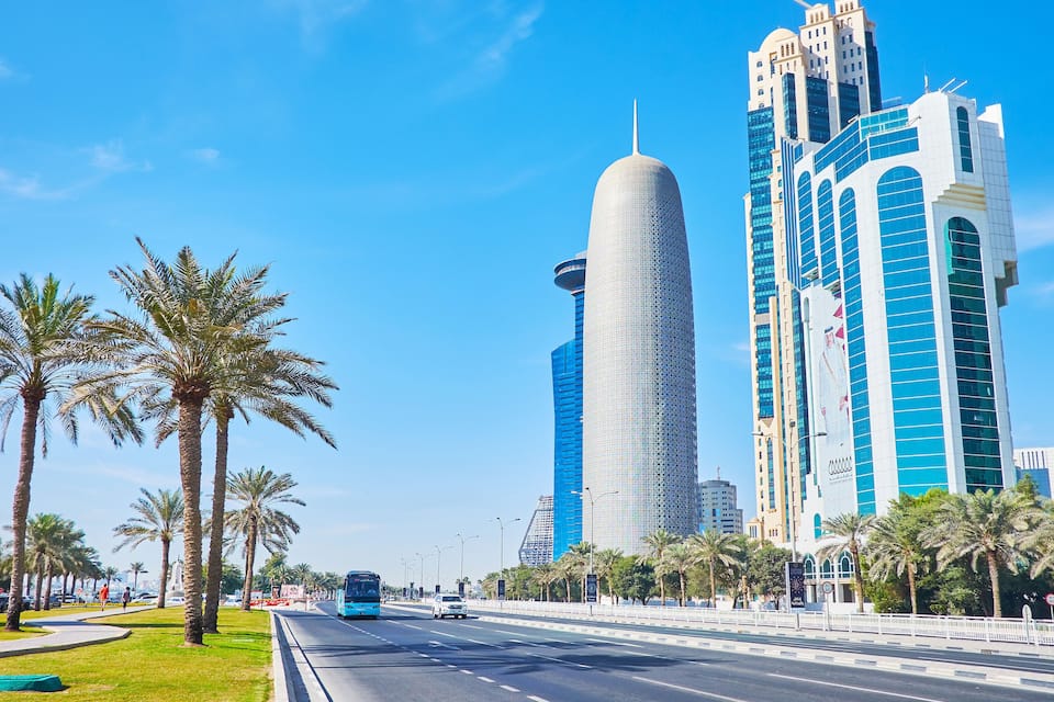 A modern cityscape with tall buildings, palm trees, and a clear blue sky.