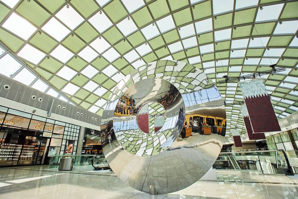 A modern shopping mall with a large glass ceiling and a spherical sculpture reflecting the interior.