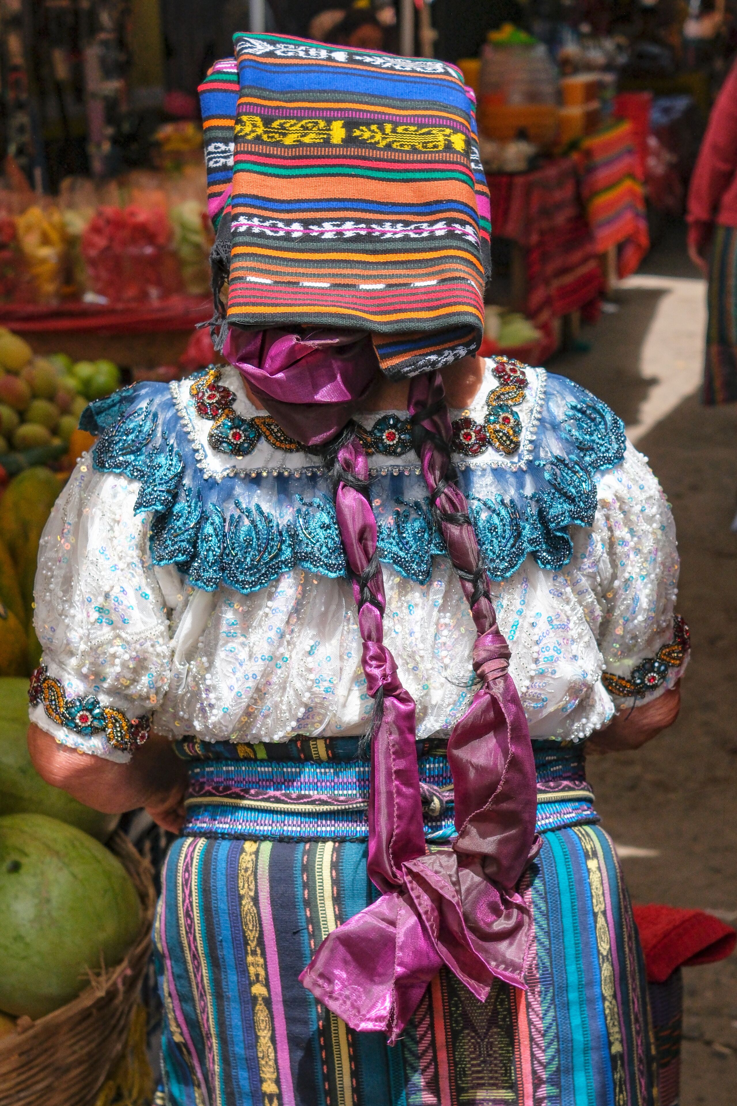 A person in traditional colorful attire with intricate patterns and a purple sash.