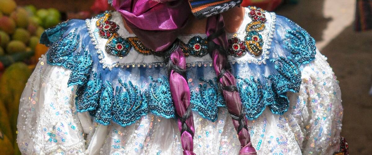 A person in traditional colorful attire with intricate patterns and a purple sash.