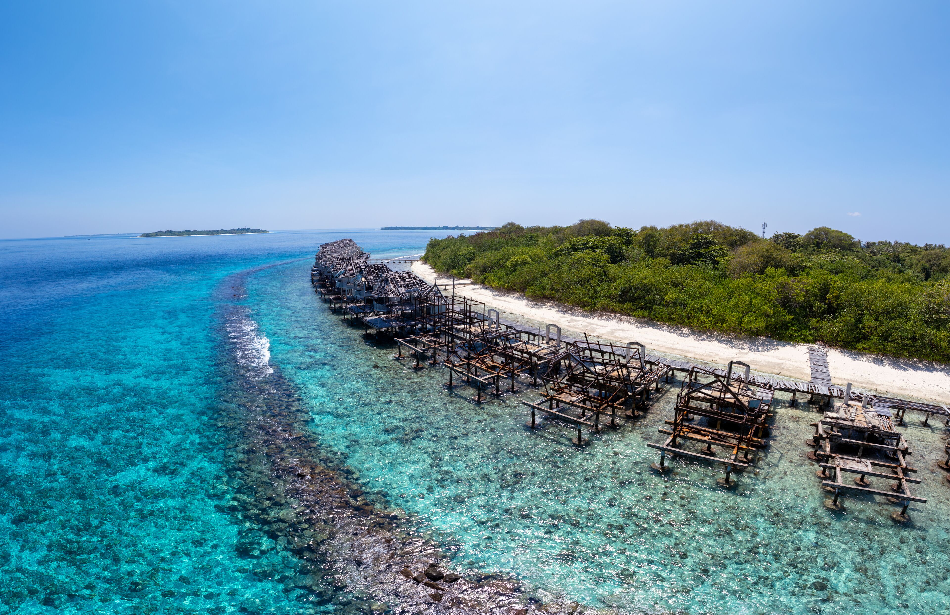 A clear turquoise sea, a wooden pier, and a sandy beach with dense greenery.