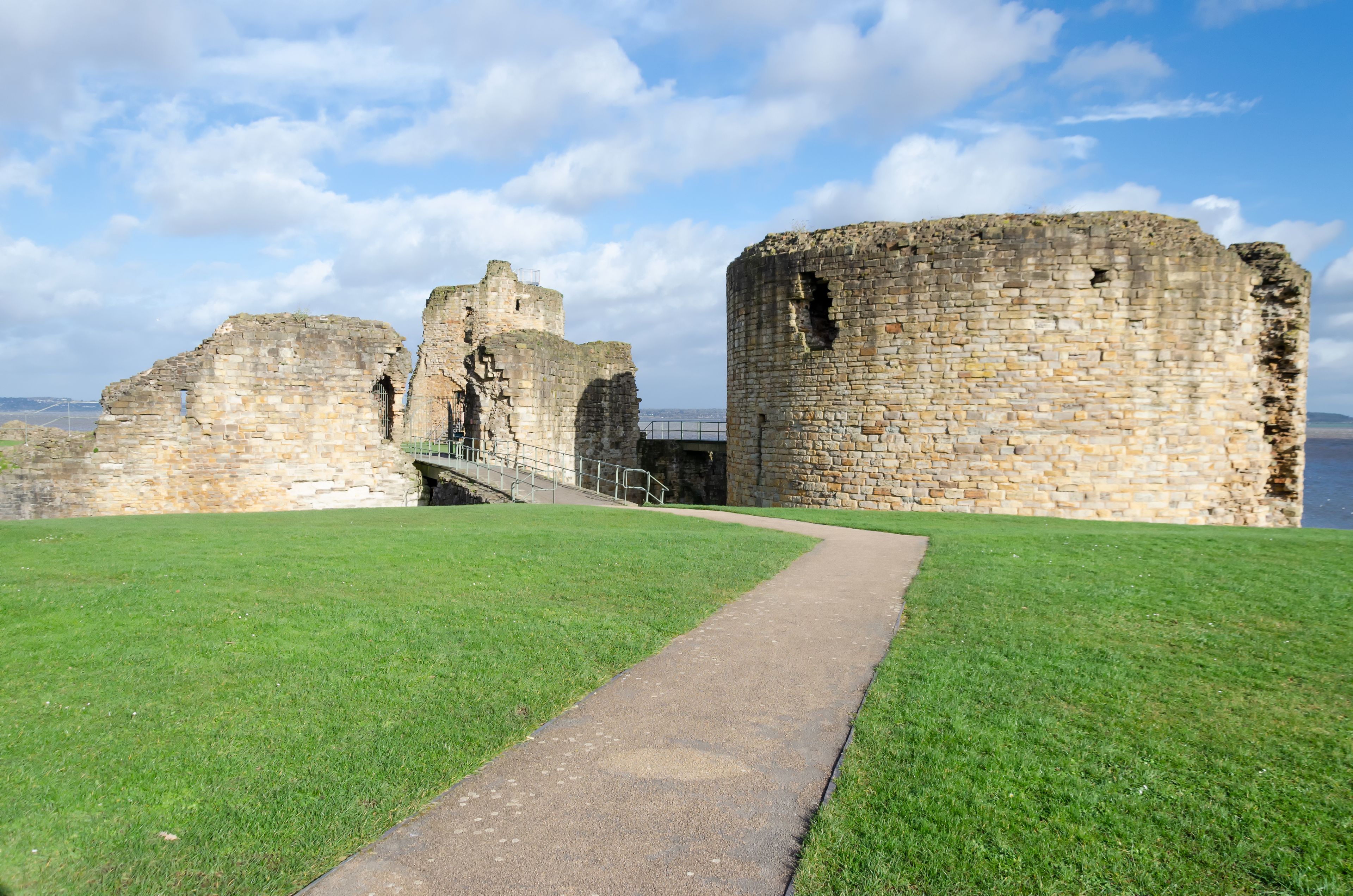 A historic stone castle ruin with a grassy foreground and a clear sky.