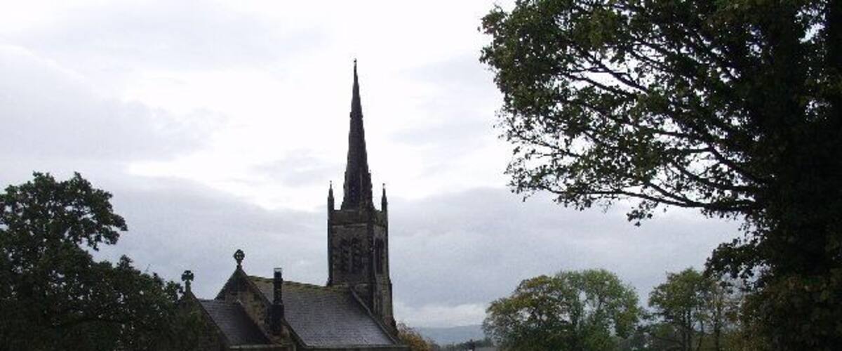 A church with a tall spire, surrounded by trees and a fence.