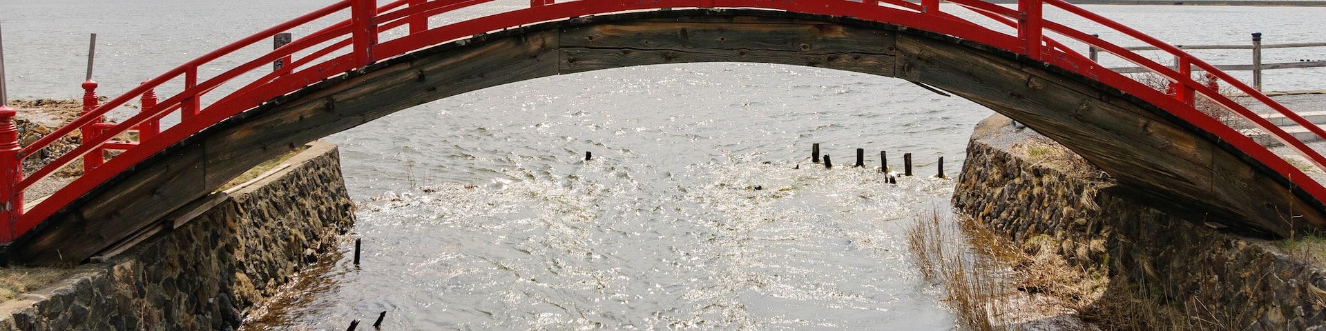Un puente rojo sobre un río helado con montañas al fondo.