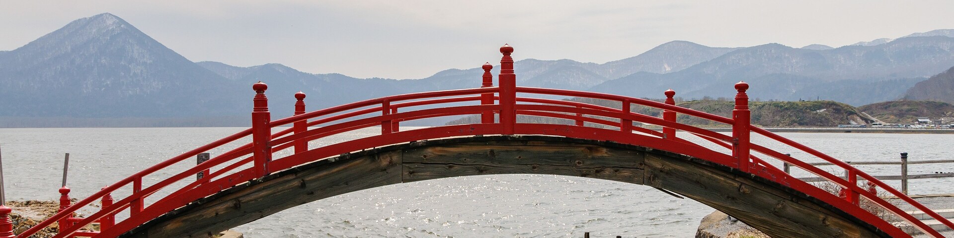 A red bridge over a frozen river with mountains in the background.