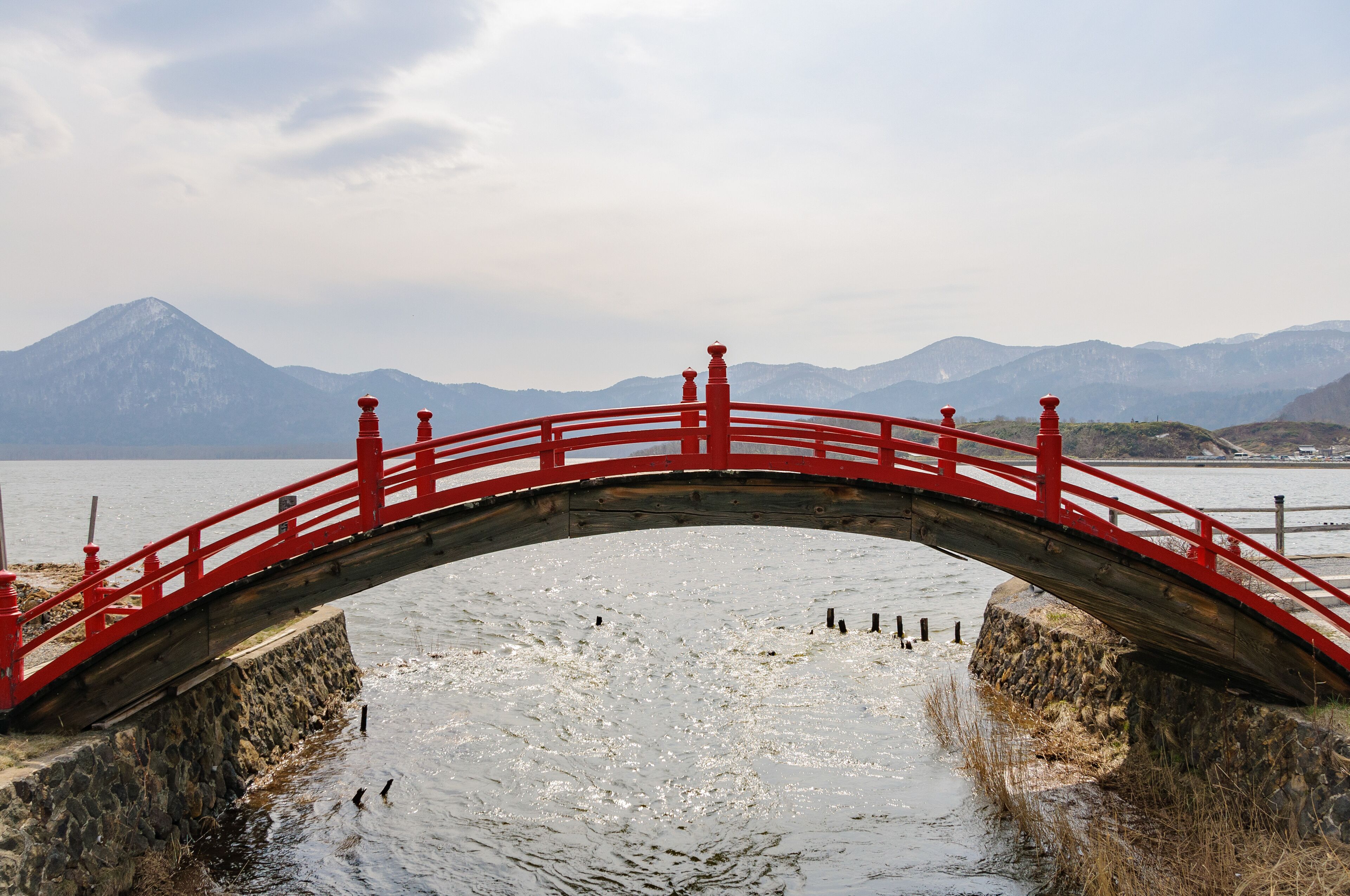 A red bridge over a frozen river with mountains in the background.