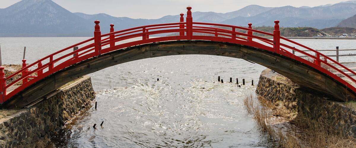 A red bridge over a frozen river with mountains in the background.