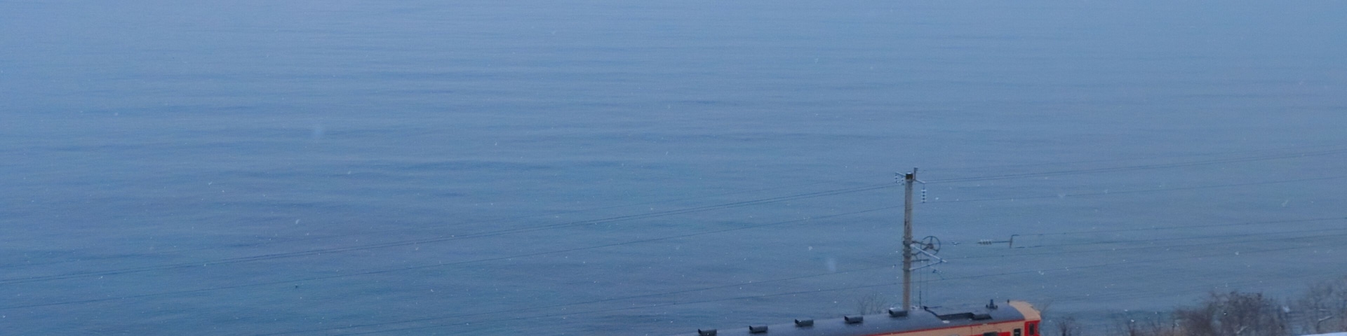 A train on tracks near a body of water with a snowy landscape.