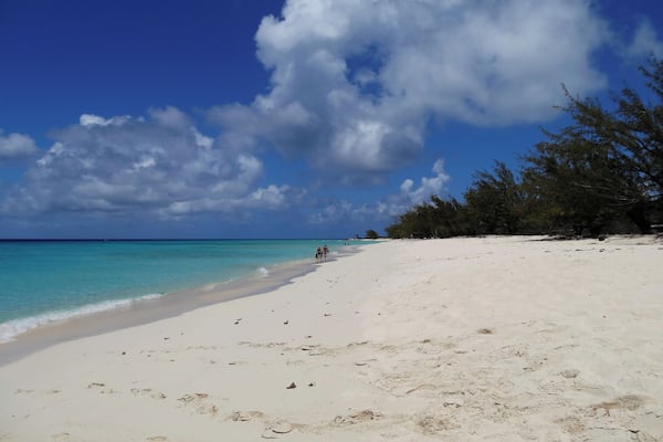 A beach with white sand, turquoise water, and a clear sky with clouds.