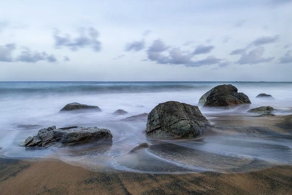 A beach with large rocks and calm water.