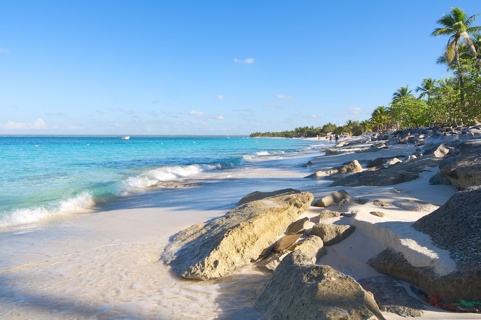 A beach with clear turquoise water, large rocks, and palm trees.