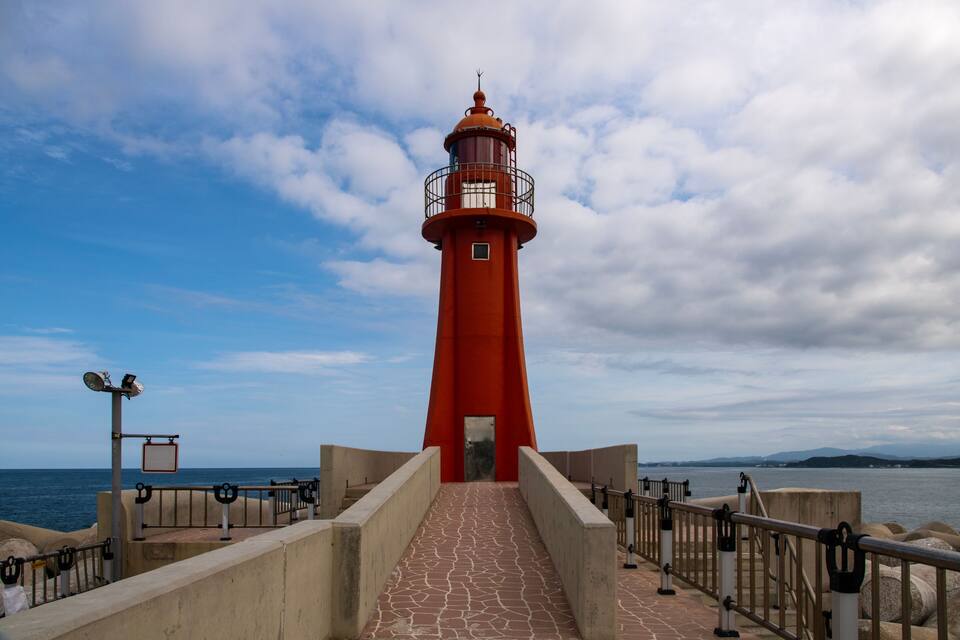 A red lighthouse with a staircase leading up to it, overlooking the sea.