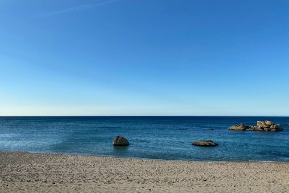 Uma praia com águas azul-claras e grandes rochas ao longe.