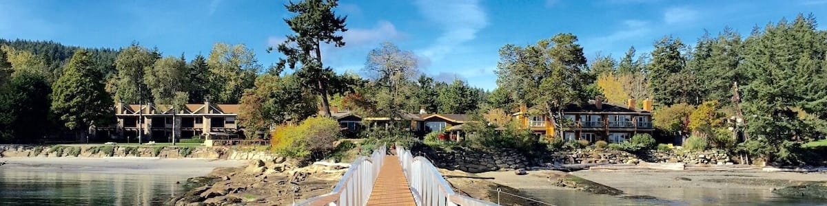 Une promenade en bois qui mène à la rive d’une rivière, avec des maisons et des arbres en arrière-plan.