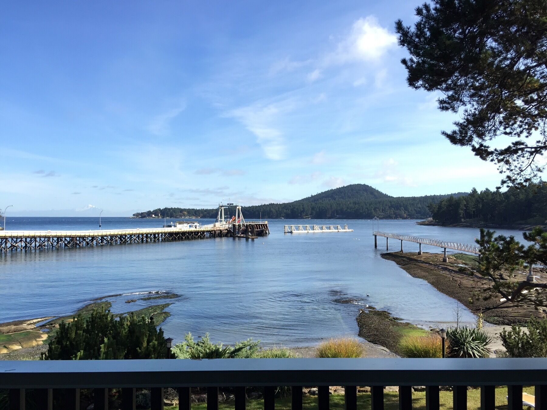 A coastal scene with a pier extending into calm waters, a small boat docked at the pier, and a bridge in the background.