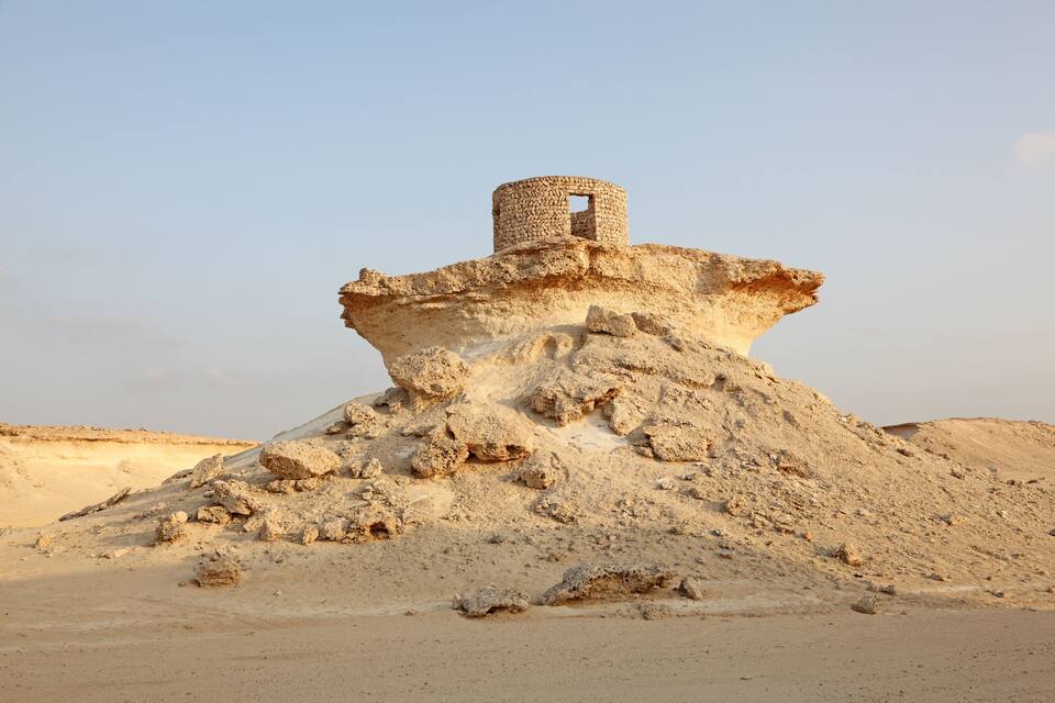 A desert landscape with a prominent rock formation featuring a cylindrical structure on top.