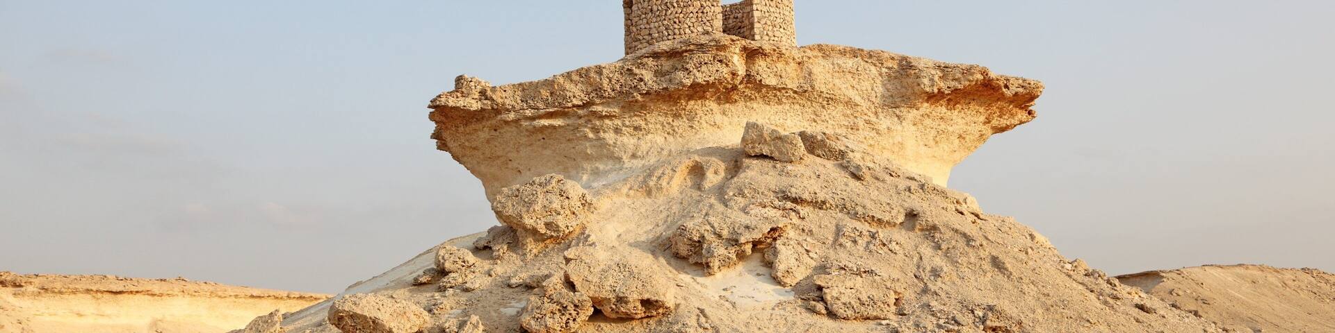 A large sand dune with a stone structure on top.