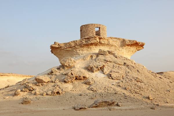 Eine große Sanddüne mit einer Steinstruktur obenauf.
