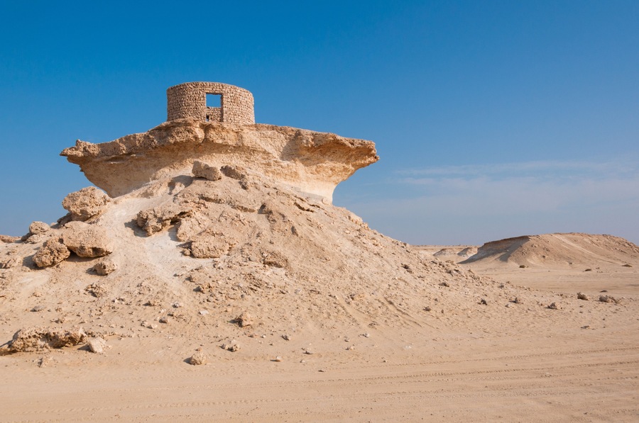 A desert landscape with a prominent rock formation featuring a cylindrical structure on top.