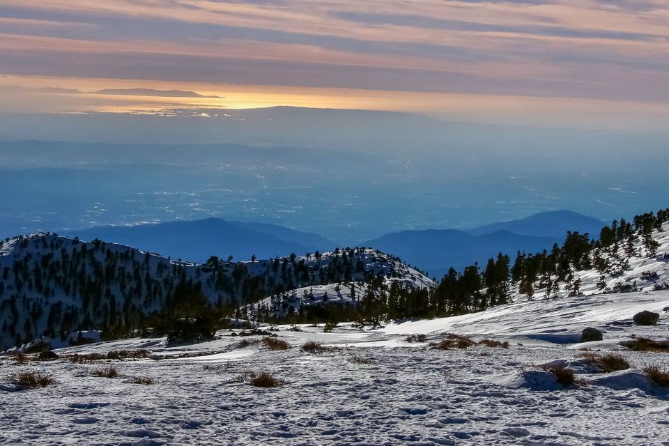 A snow-covered mountain range with a sunset in the background.