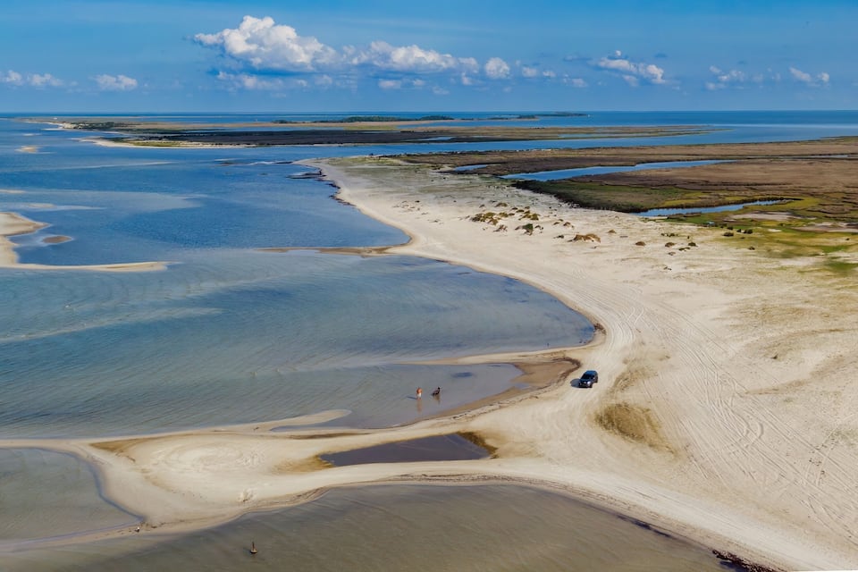 A coastal landscape with a sandy beach, tidal flats, and a clear blue sky.