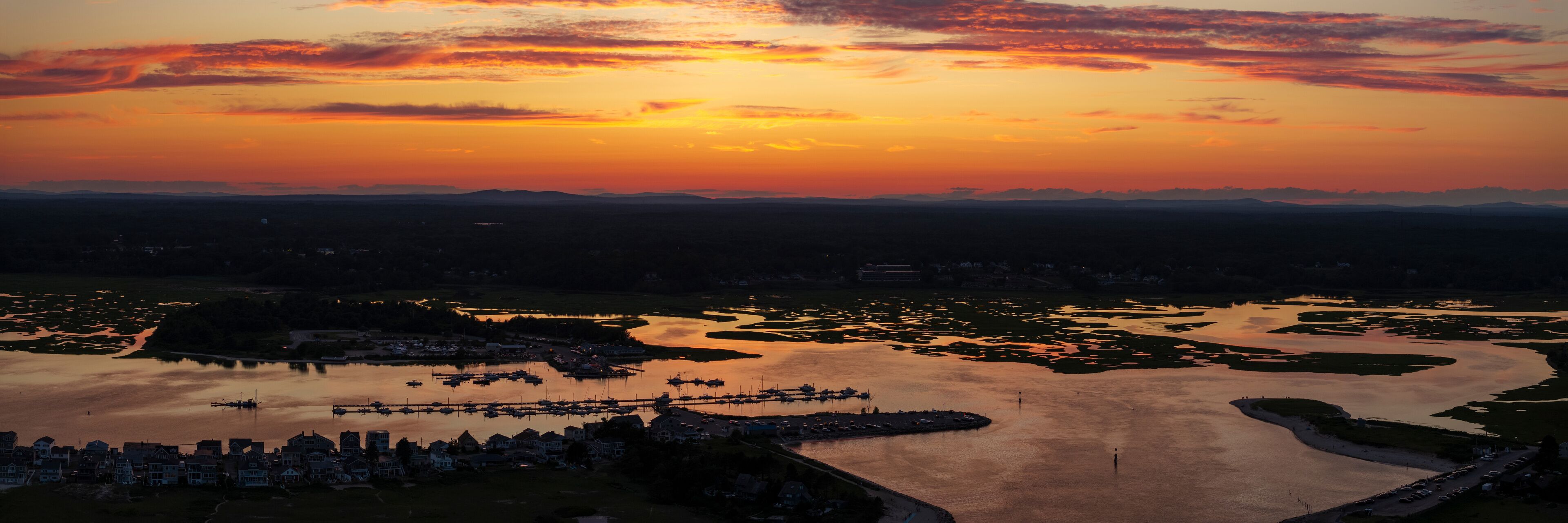 Aerial view of serene sunset over the coast with boats at the dock and majestic mountains in the background, Wells, United States.