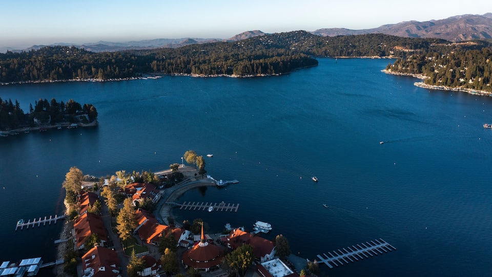 A lake surrounded by forested hills, a pier, and a small village with red-roofed buildings.