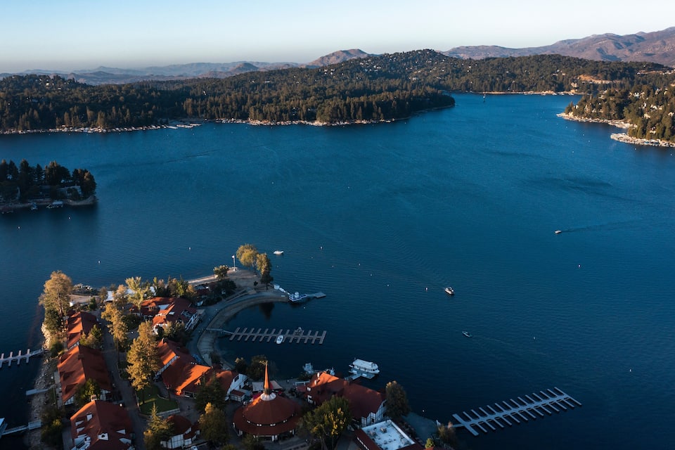 A lake surrounded by forested hills, a pier, and a small village with red-roofed buildings.
