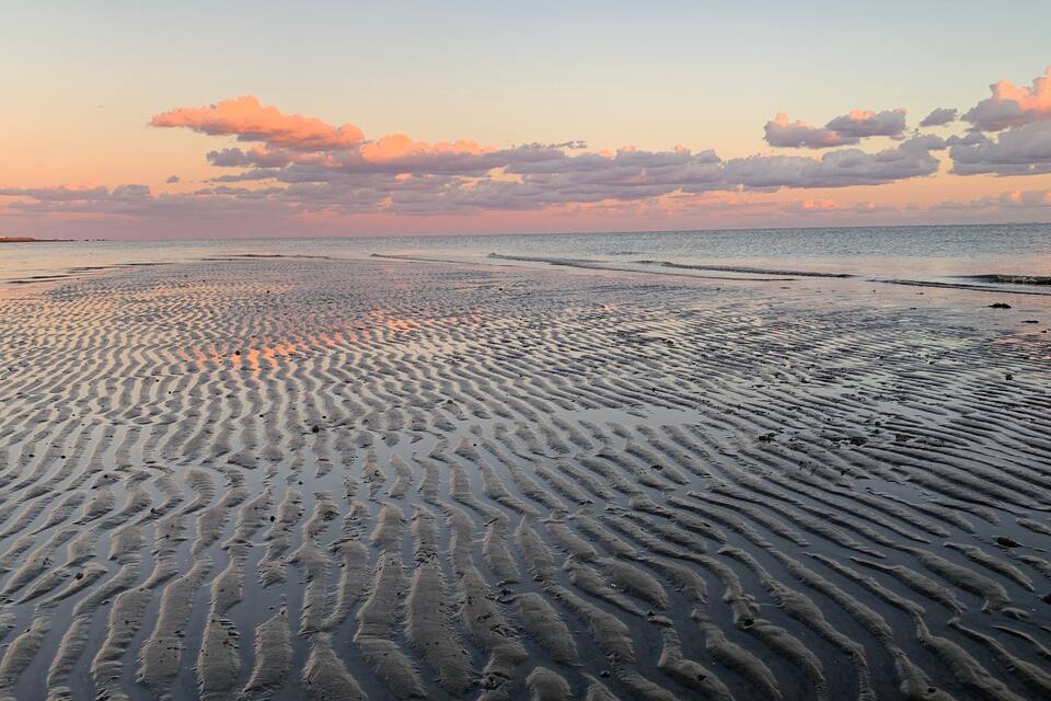 Una playa con patrones ondulados en la arena y un cielo al atardecer.
