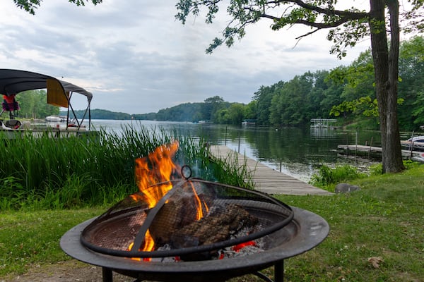 Campfire on the shore with docks, pontoon boat, and lake in the background.