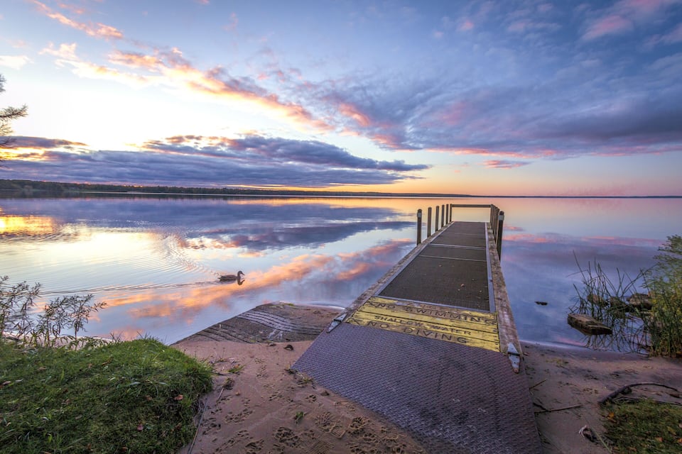 A pier extending into calm water with a sunset sky.