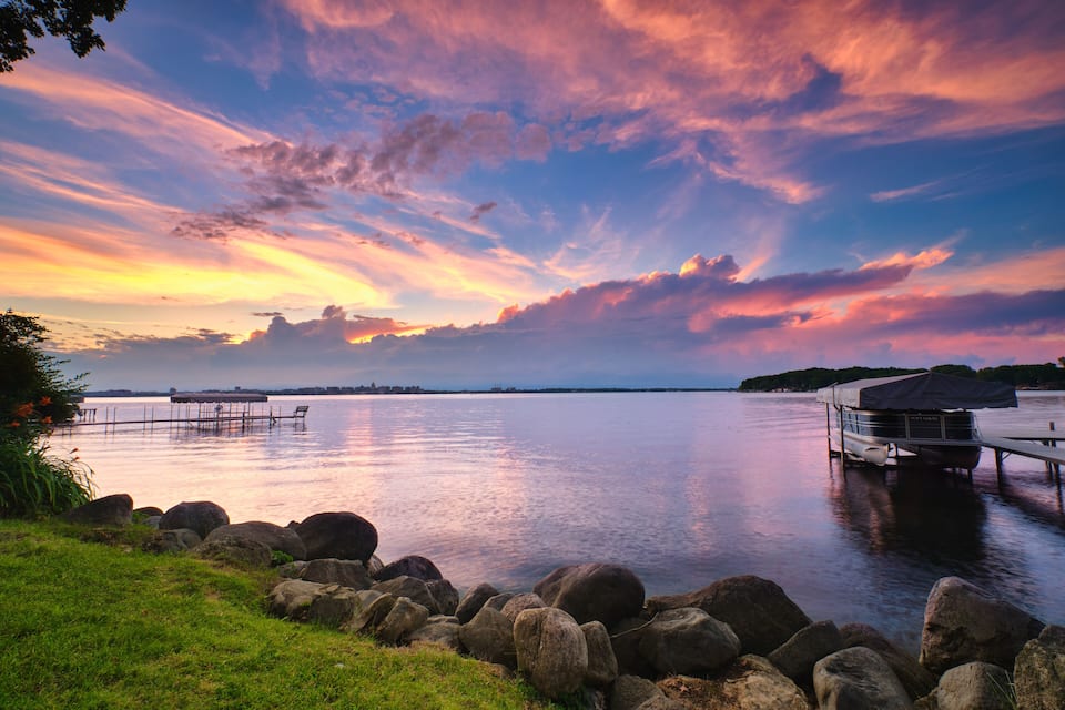 Un lac paisible au coucher du soleil, avec un quai et un bateau à l’abri.