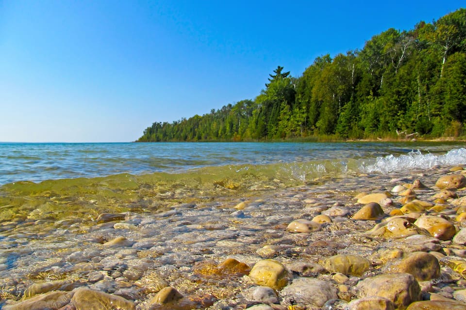 A clear lake with visible rocks and a forested shoreline.