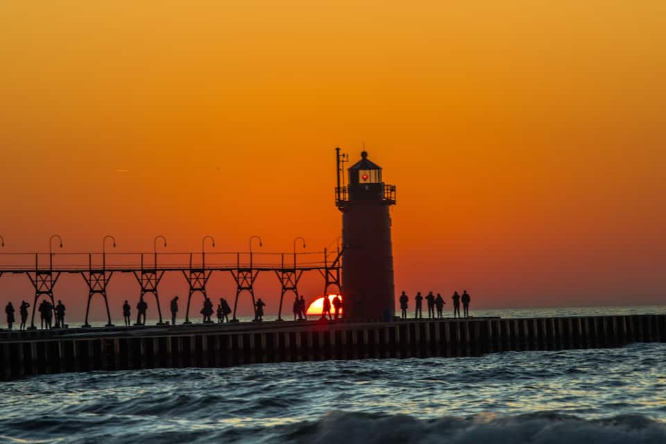 A lighthouse at sunset with people on a pier.