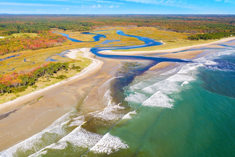 An aerial view of a coastal area with a river delta, sandy beaches, and a forested landscape.