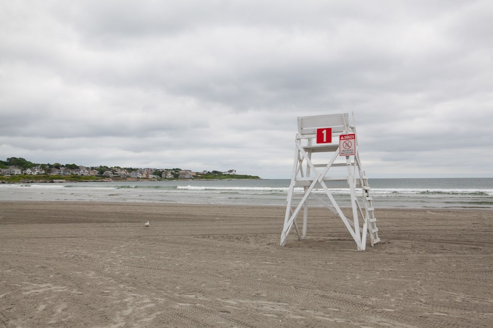 A lifeguard tower on a beach with a cloudy sky and ocean waves in the background.