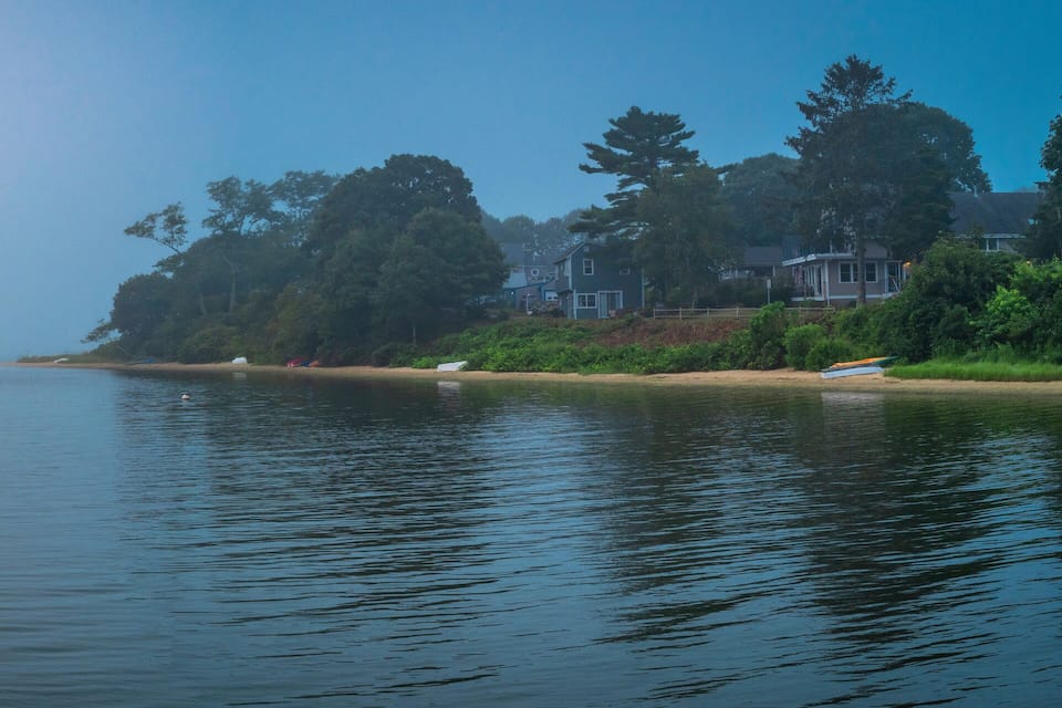A calm lake with boats, a sandy shore, and houses along the edge.
