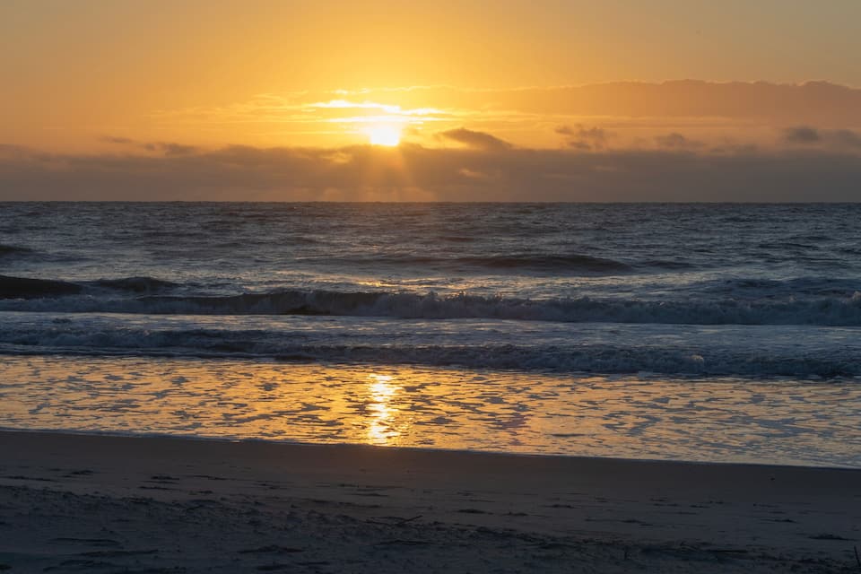 A sunset over the ocean with waves on the shore.