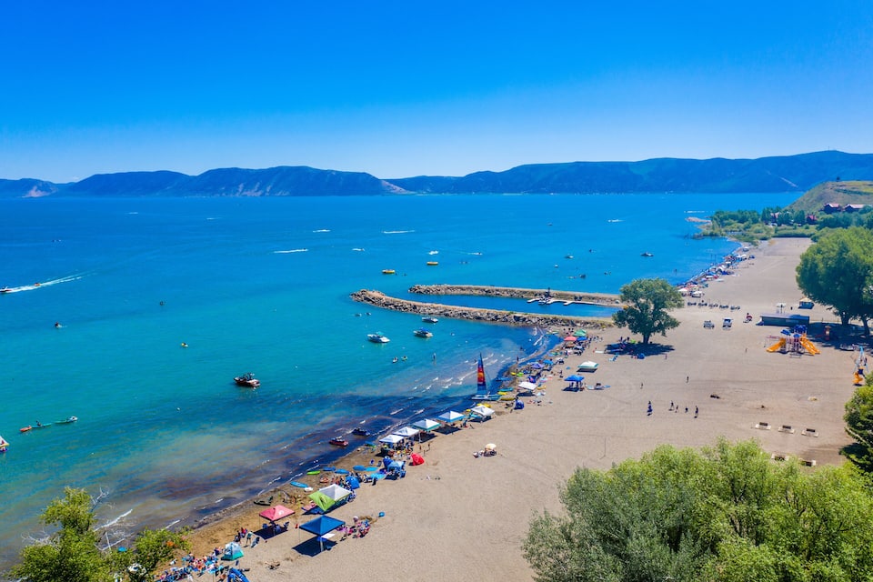 A coastal beach with clear turquoise waters, boats, and beach umbrellas.