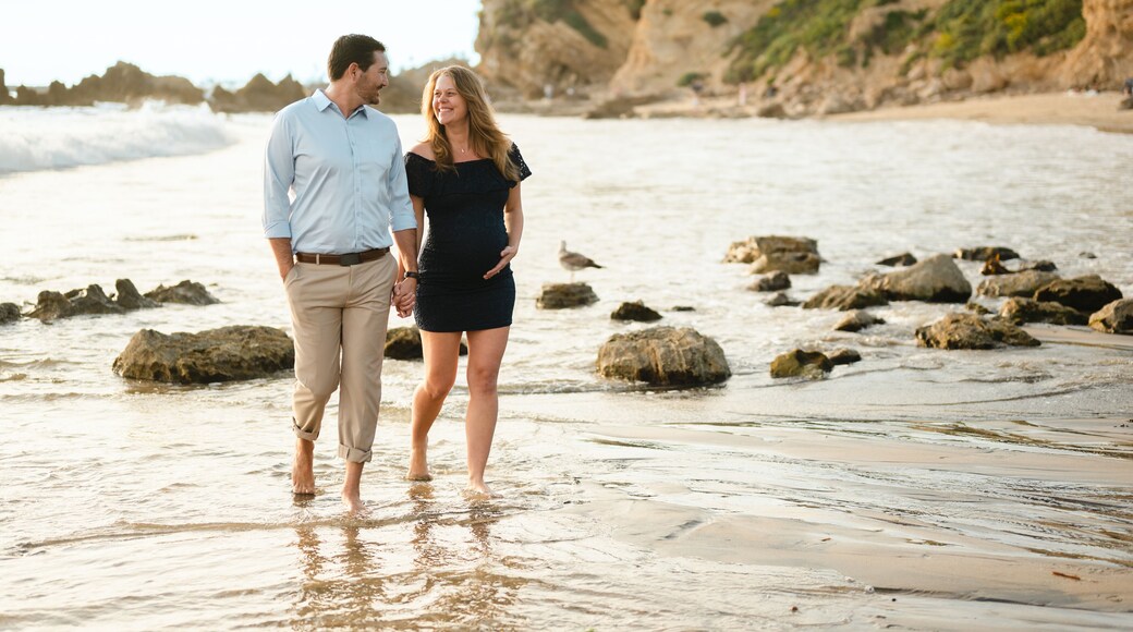 Beautiful pregnant couple walking along the coastal beach shore