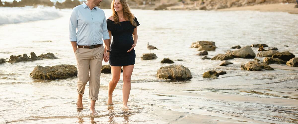 Beautiful pregnant couple walking along the coastal beach shore