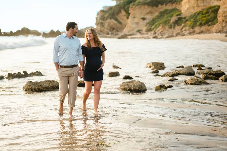 A couple walking on a rocky beach with waves crashing nearby.